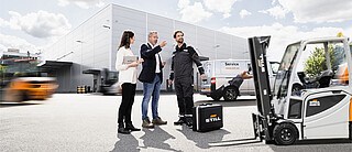 Drei Menschen stehen vor eine STILL-Lager. Um sie herum mehrere Gabelstapler von STILL.