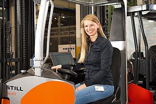 Eine Person sitzt in einem STILL Gabelstapler und lächelt in die Kamera.