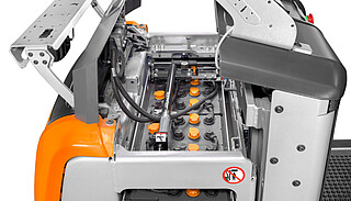 Close-up of an open battery compartment on a forklift, showing a large battery with many yellow cell caps.